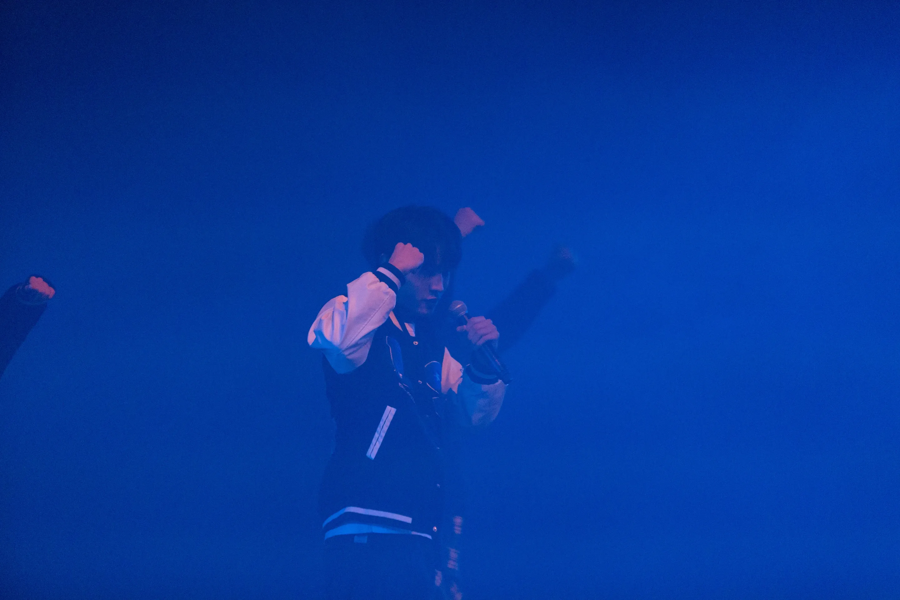 Jeffrey Lin under blue stage lighting, holding a microphone.