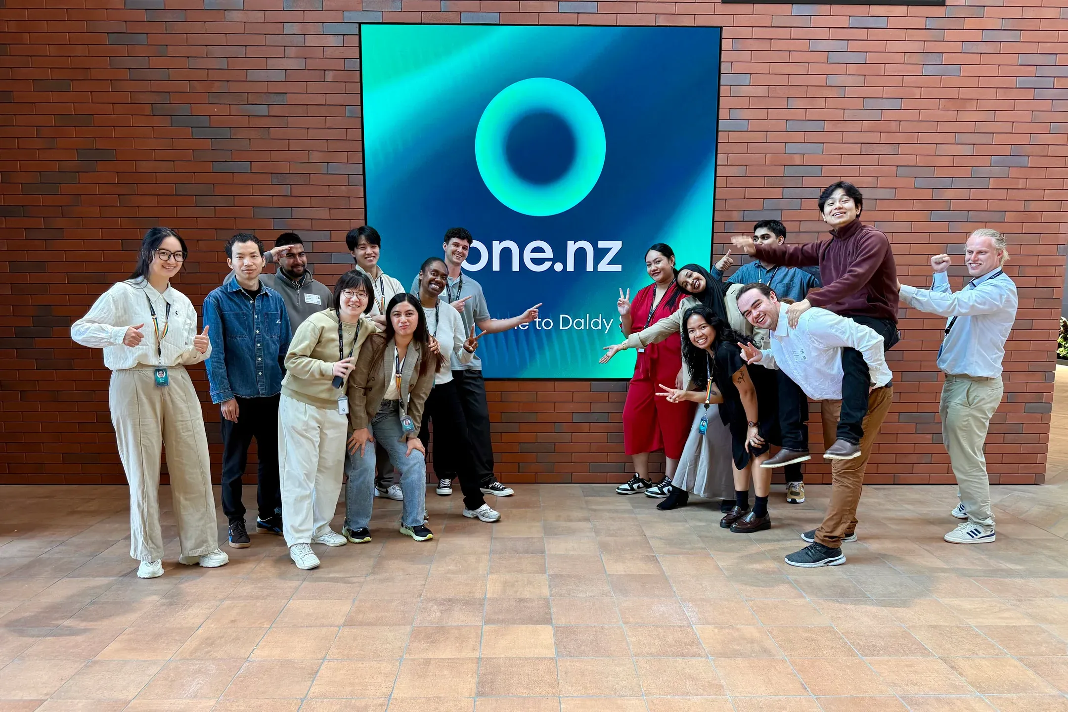 Jeffrey Lin with a group of colleagues posing in front of a large one.nz sign.