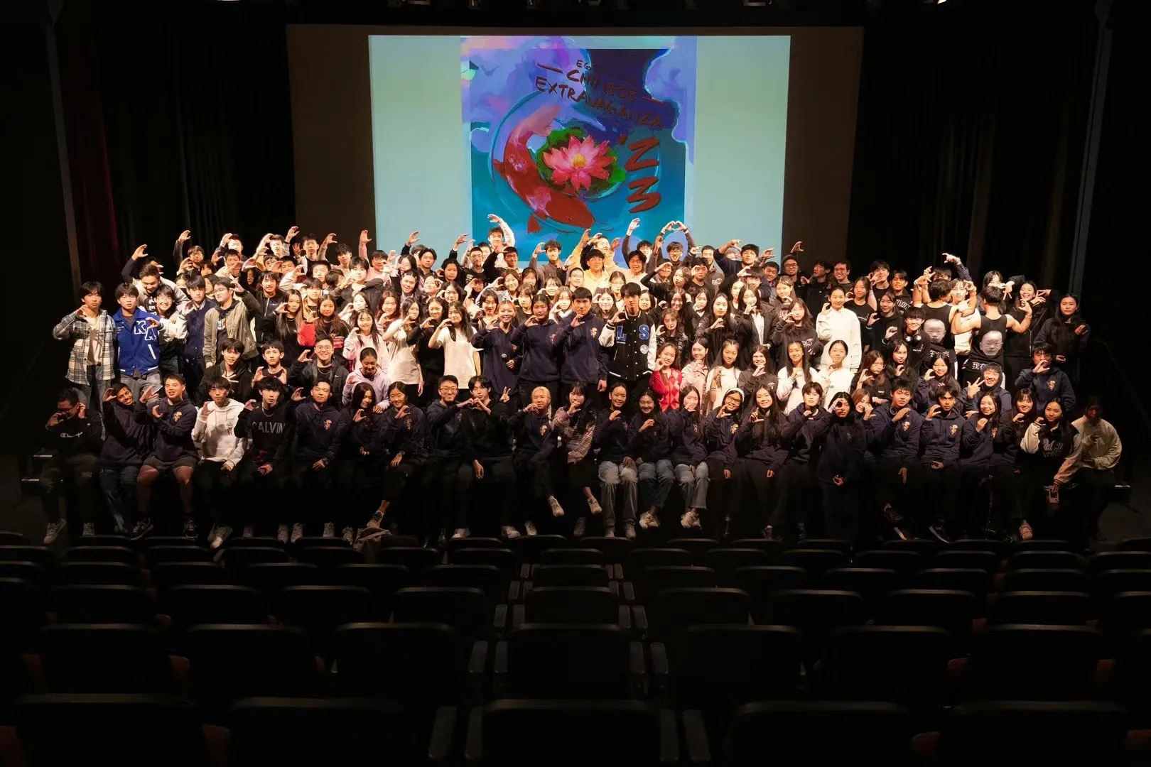 A large performance cast gathered on an auditorium stage.