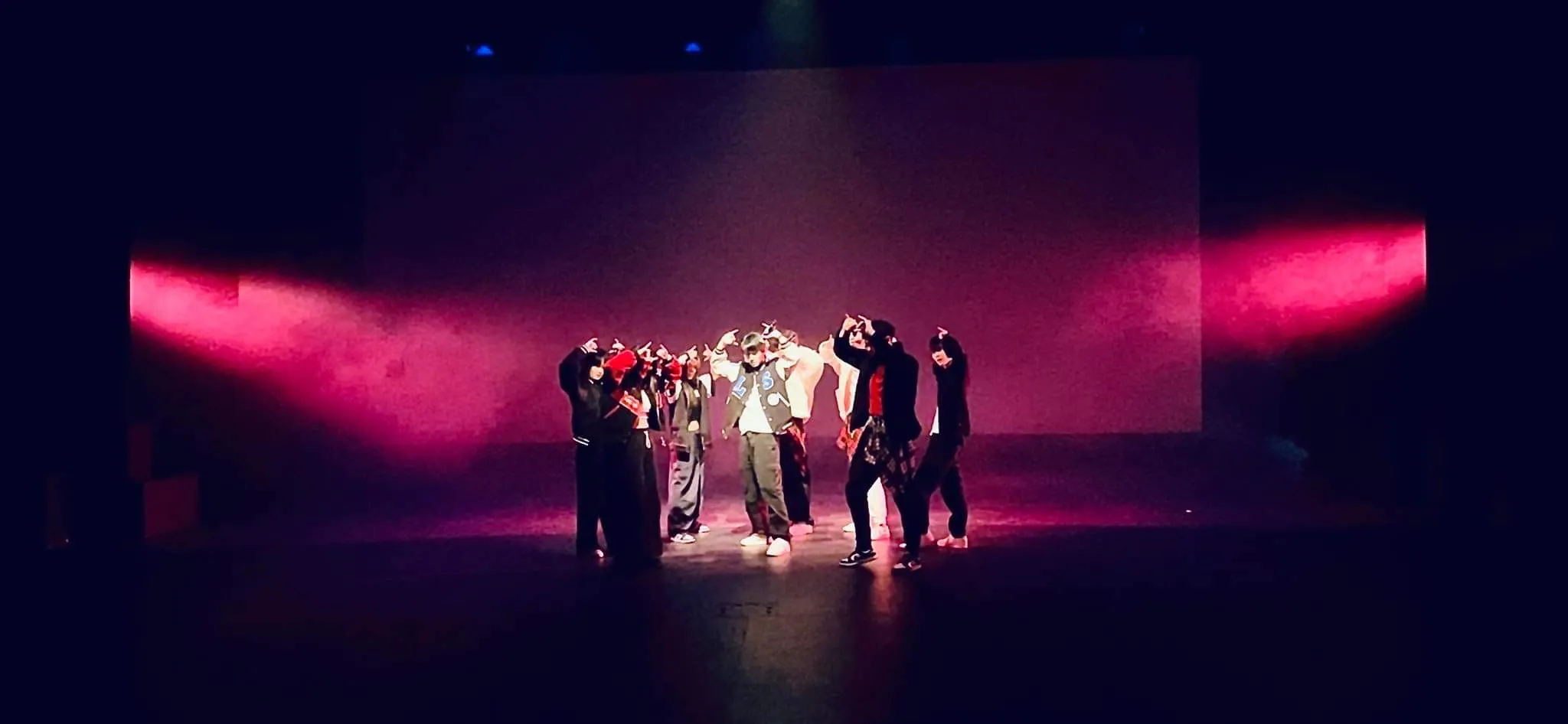 A wide ensemble performance on stage under vivid theatrical lighting.